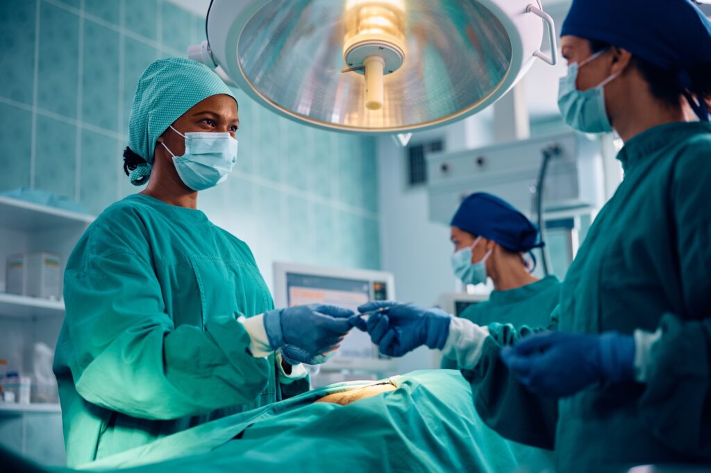 Medical technician assisting black female doctor during a surgery at medical clinic.